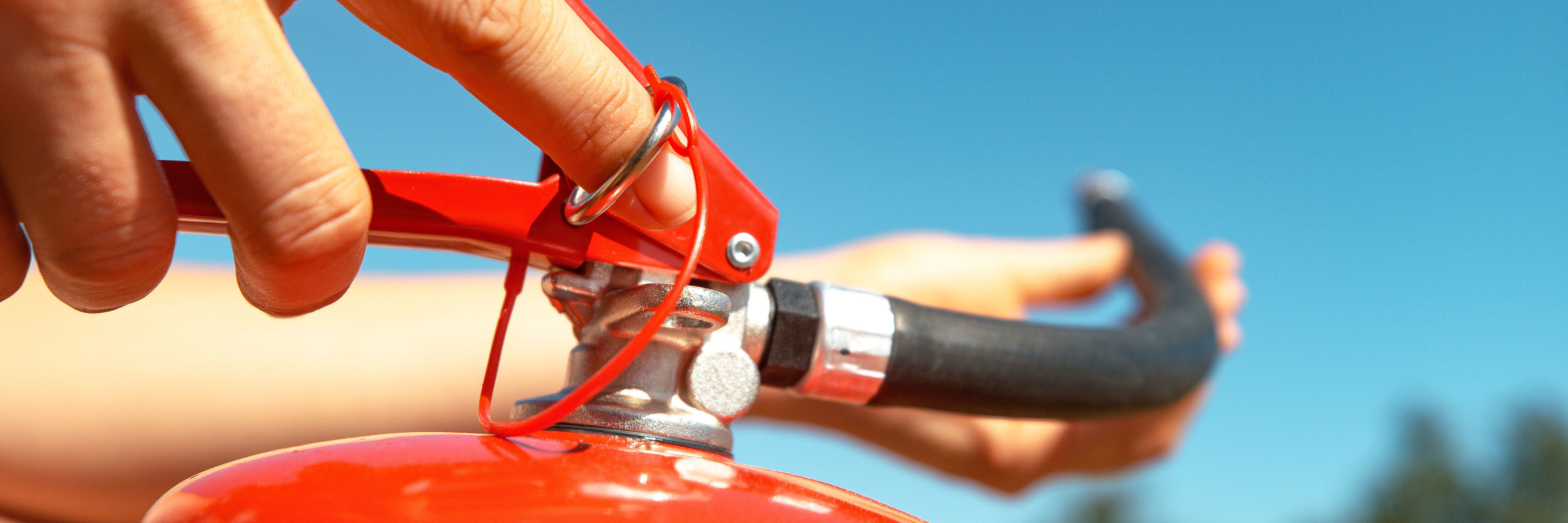 MACRO: Young woman pulls safety pin out of a fire extinguisher b
